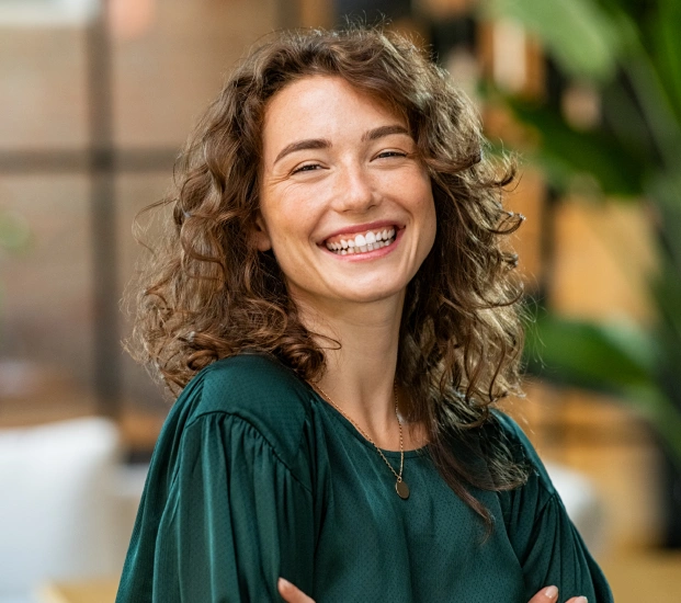 Young woman smiling at camera wearing green shirt in bright dental office setting.