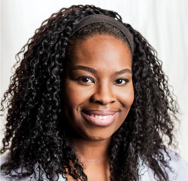 Professional headshot of smiling woman with long dark curly hair against white background.