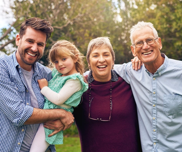 Multi-generational family smiling together outdoors in a green park setting.